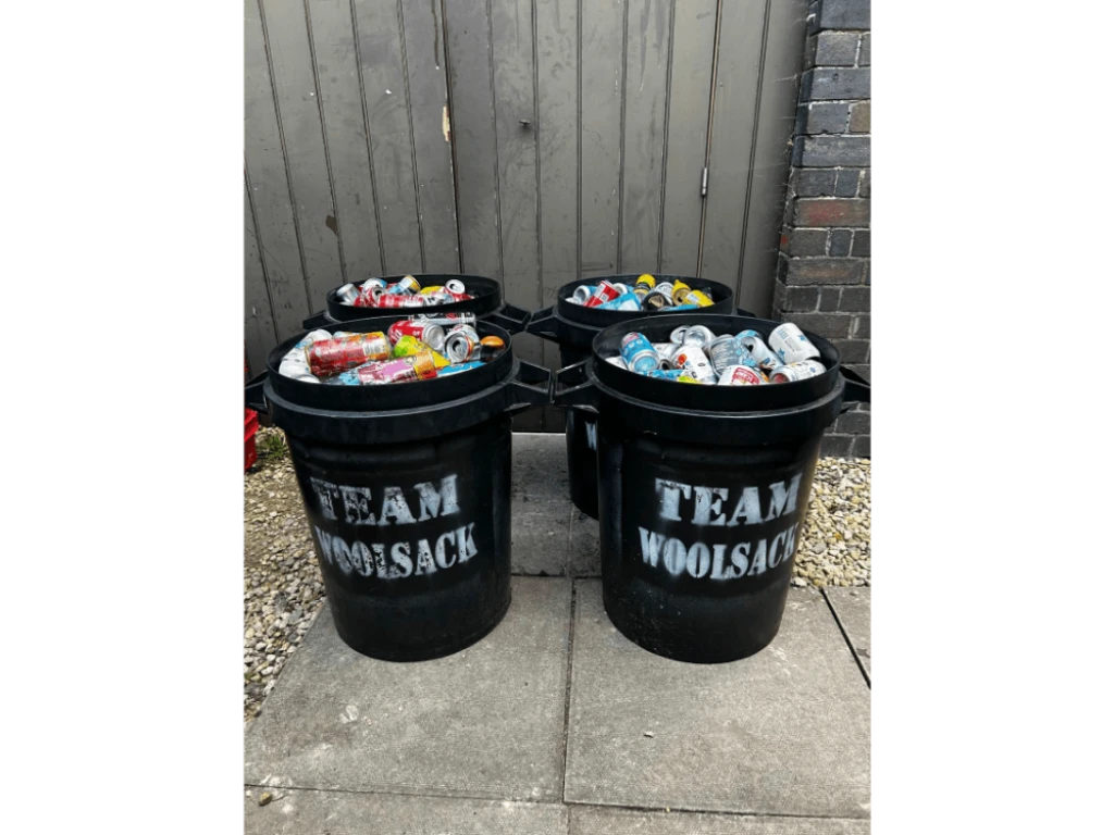 Four black Team Woolsack bins filled to the brim with aluminium drinks cans, sorted and ready for recycling