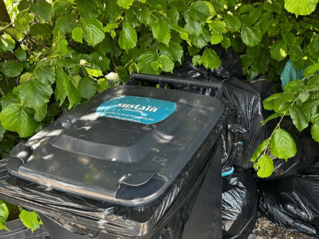 A green recycling wheelie bin held at a storage point ready for later collection